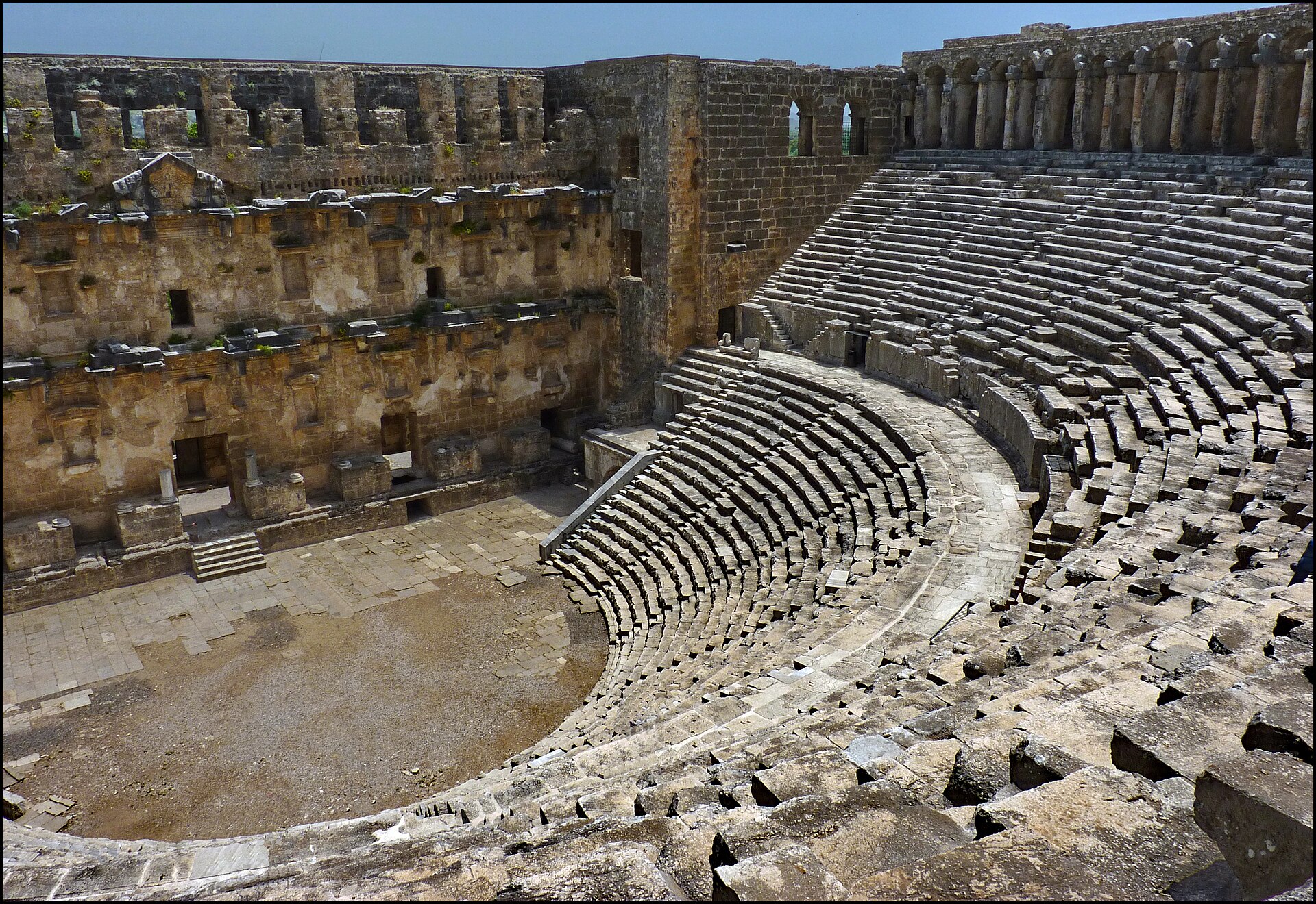 The Roman theatre of Aspendos: the semicircular stone seating and the tall, almost intact two-storey stage building in warm limestone under a blue sky.