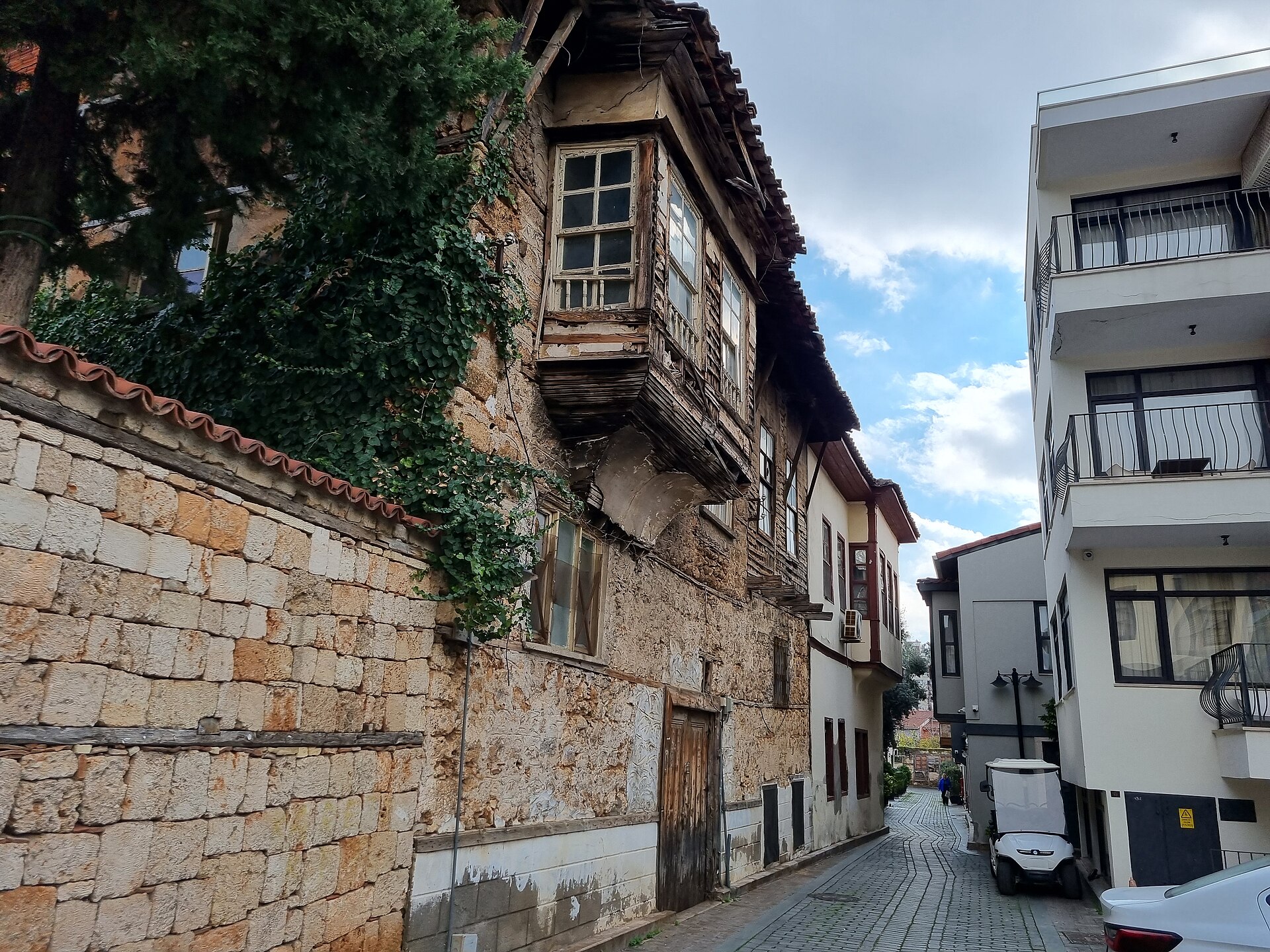 A narrow lane in Kaleiçi, Antalya: whitewashed Ottoman houses with timber frames and tile roofs, bougainvillea over the walls.
