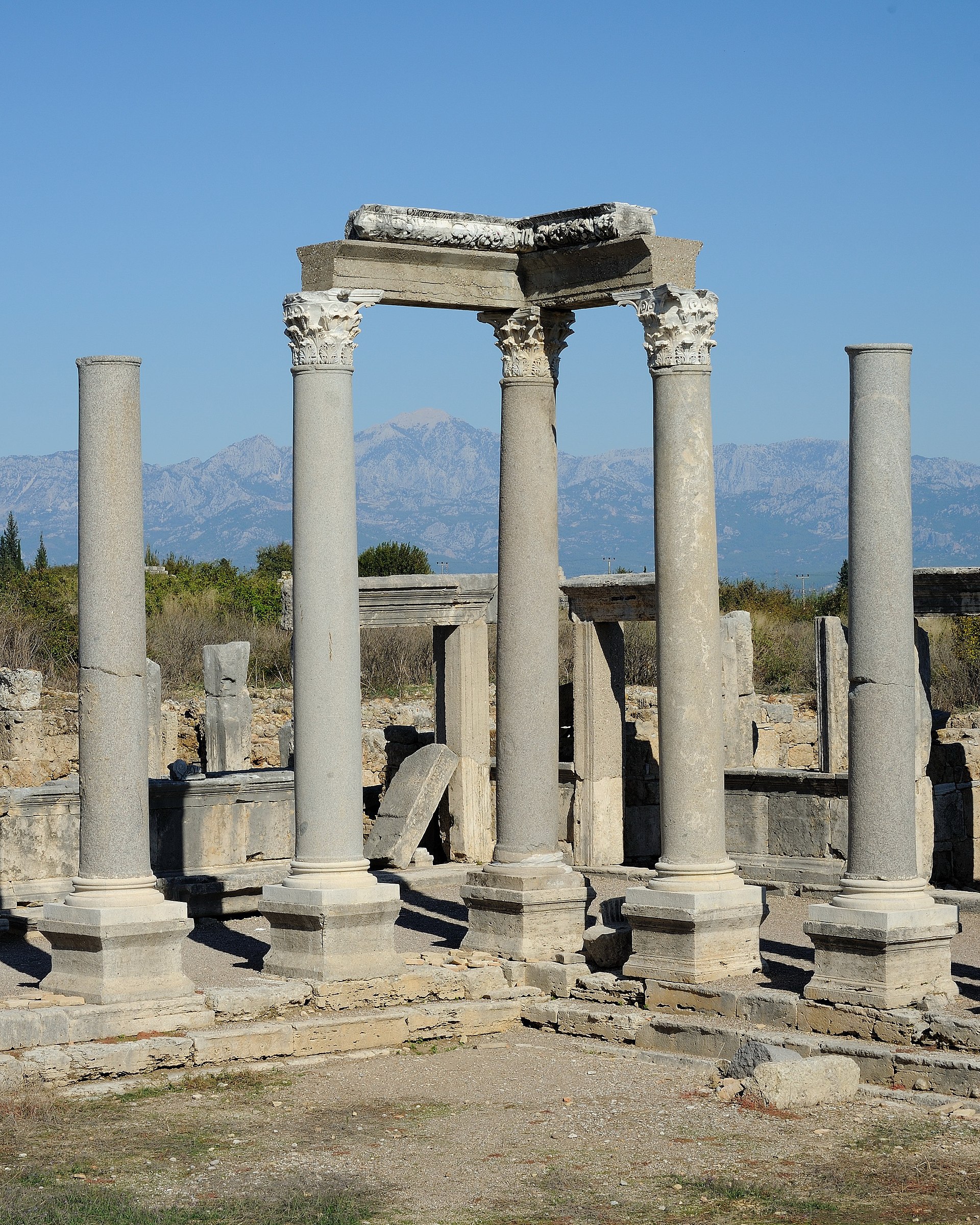 Corinthian columns and a carved entablature at the ancient city of Perge, with the blue Taurus mountains hazy behind.